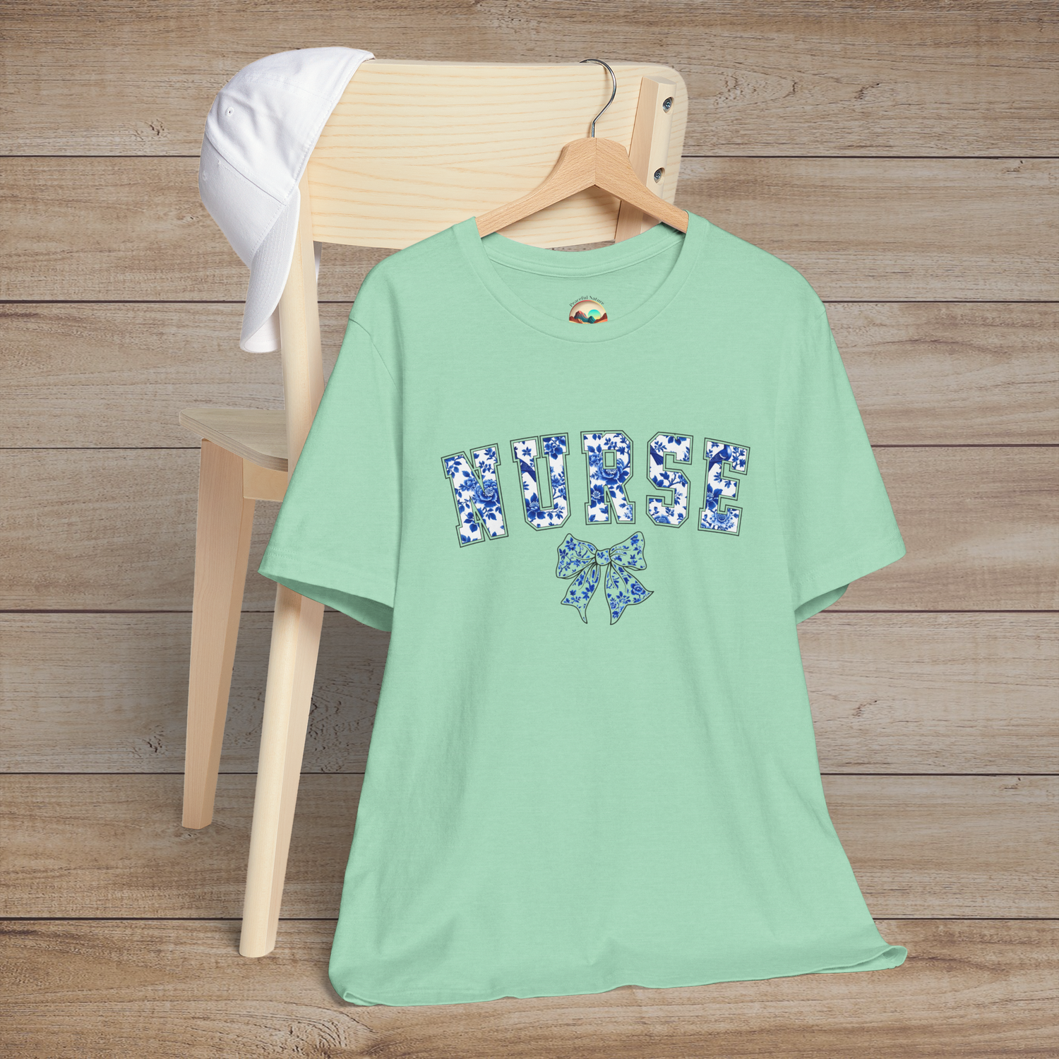 Heather mint green nurse t-shirt with delicate blue floral 'NURSE' lettering and a bow design, ideal for a soft yet strong professional look
