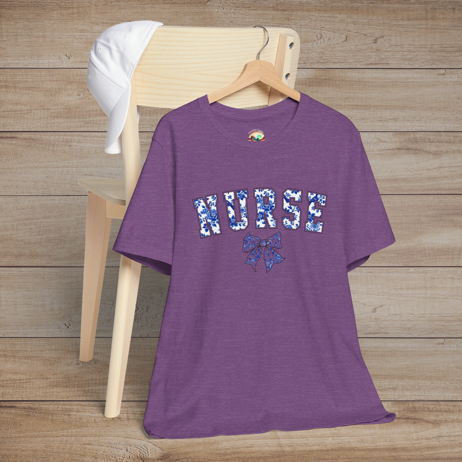 Heather purple nursing tee with floral 'NURSE' text and an elegant bow, hung stylishly on a chair – designed for proud and graceful nurses