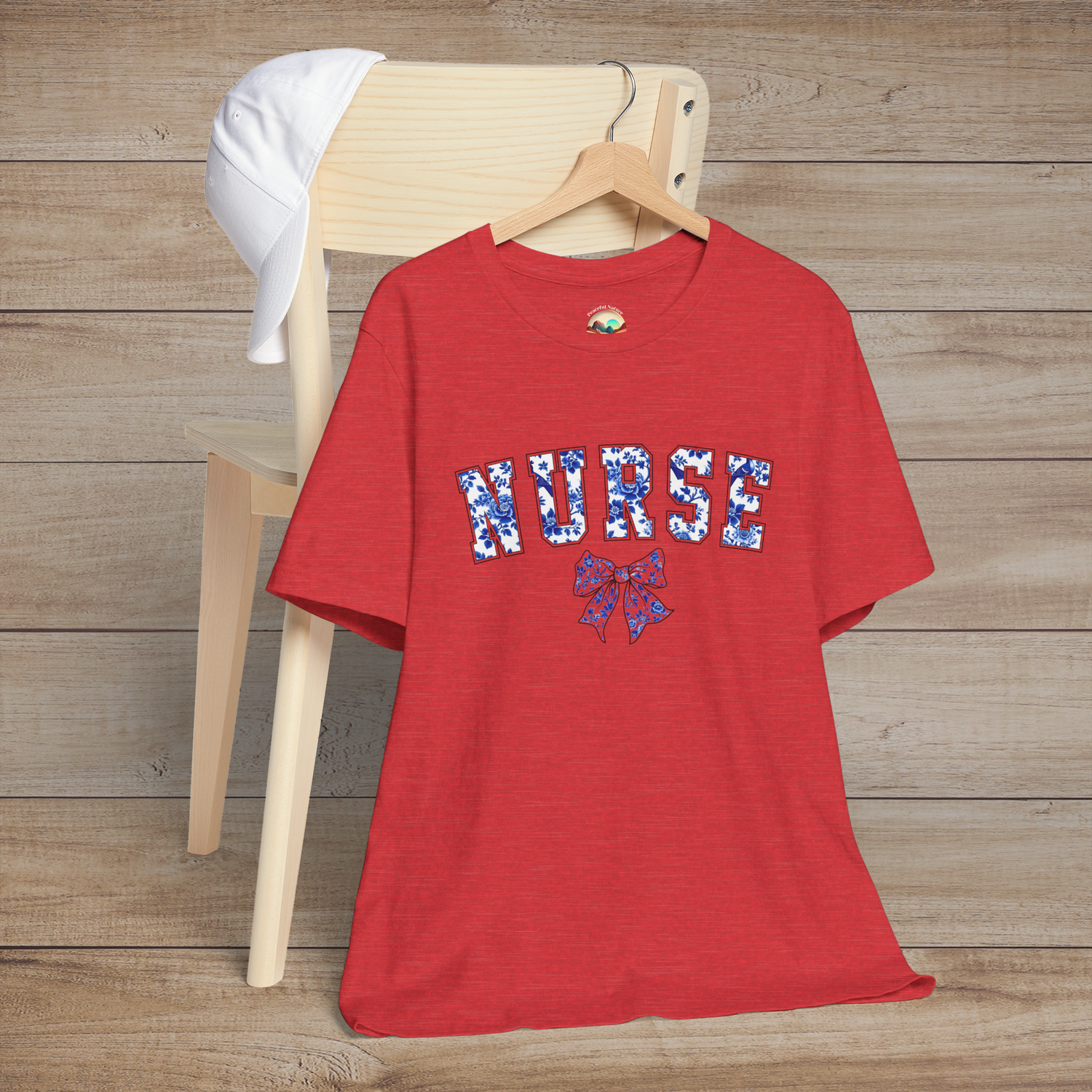 Heather red t-shirt displayed on a hanger over a chair, with bold 'NURSE' floral lettering and a decorative bow – perfect for fashionable nurses