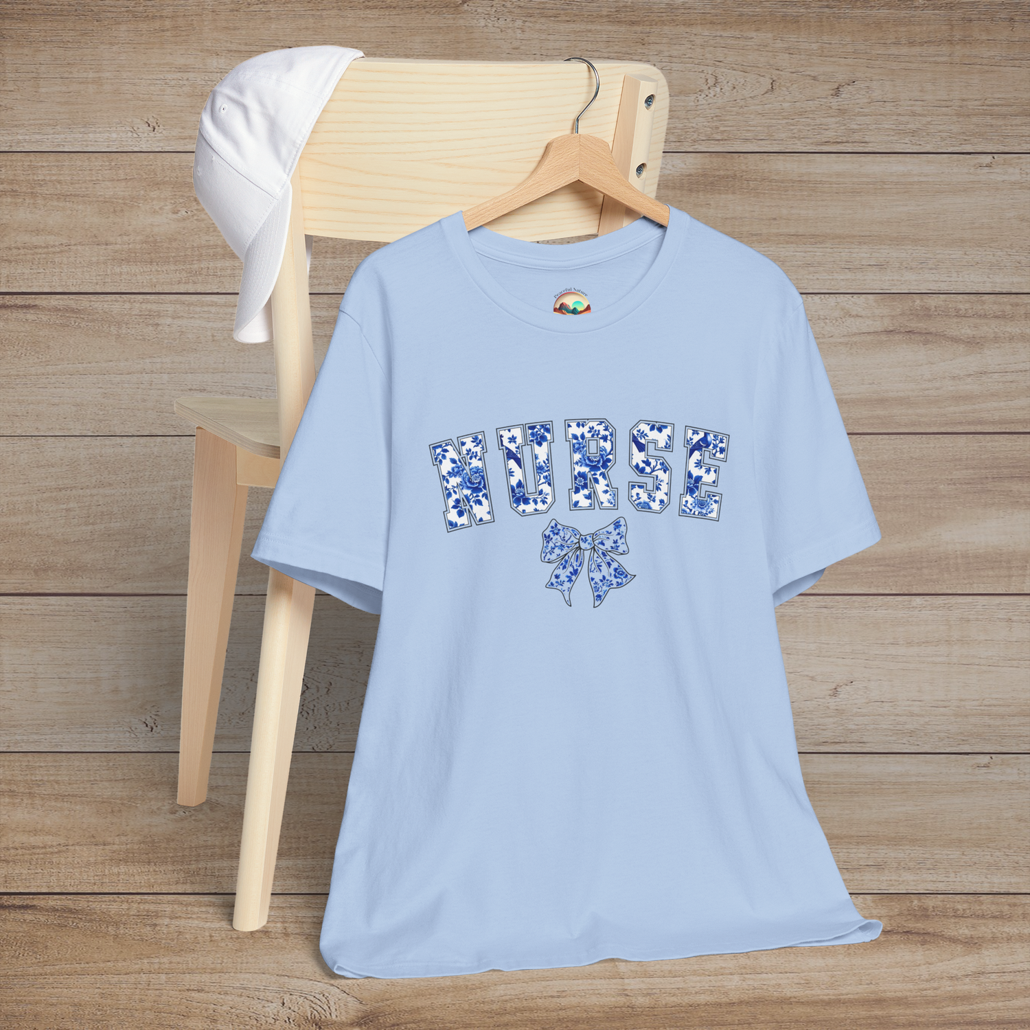 Light blue floral nurse t-shirt draped over a chair, showcasing the word 'NURSE' in bold flower-filled letters and a coordinating bow beneath