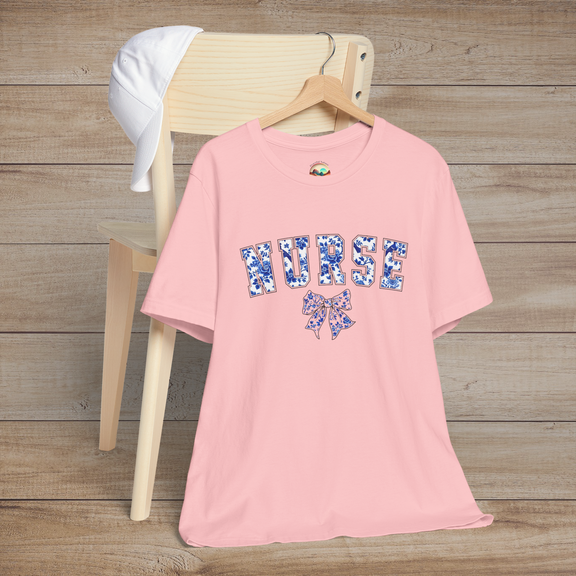 Light pink t-shirt with feminine floral 'NURSE' typography and matching bow, photographed on a hanger – perfect for nurses with a chic style