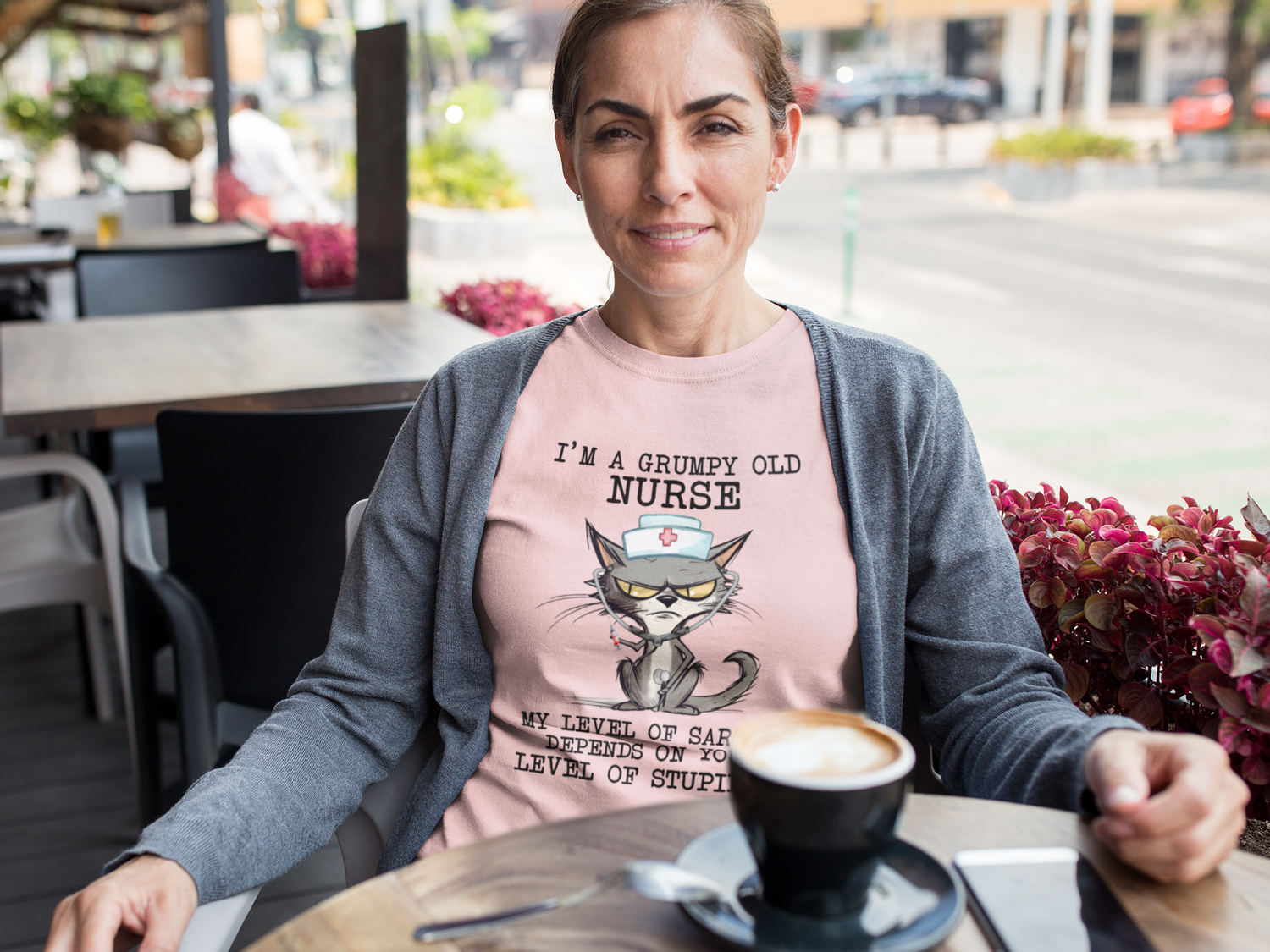 Woman relaxing at outdoor cafe wearing Funny Nurse T-Shirt with cranky cat nurse graphic and sarcasm quote, premium pink cotton fabric