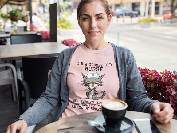 Woman relaxing at outdoor cafe wearing Funny Nurse T-Shirt with cranky cat nurse graphic and sarcasm quote, premium pink cotton fabric