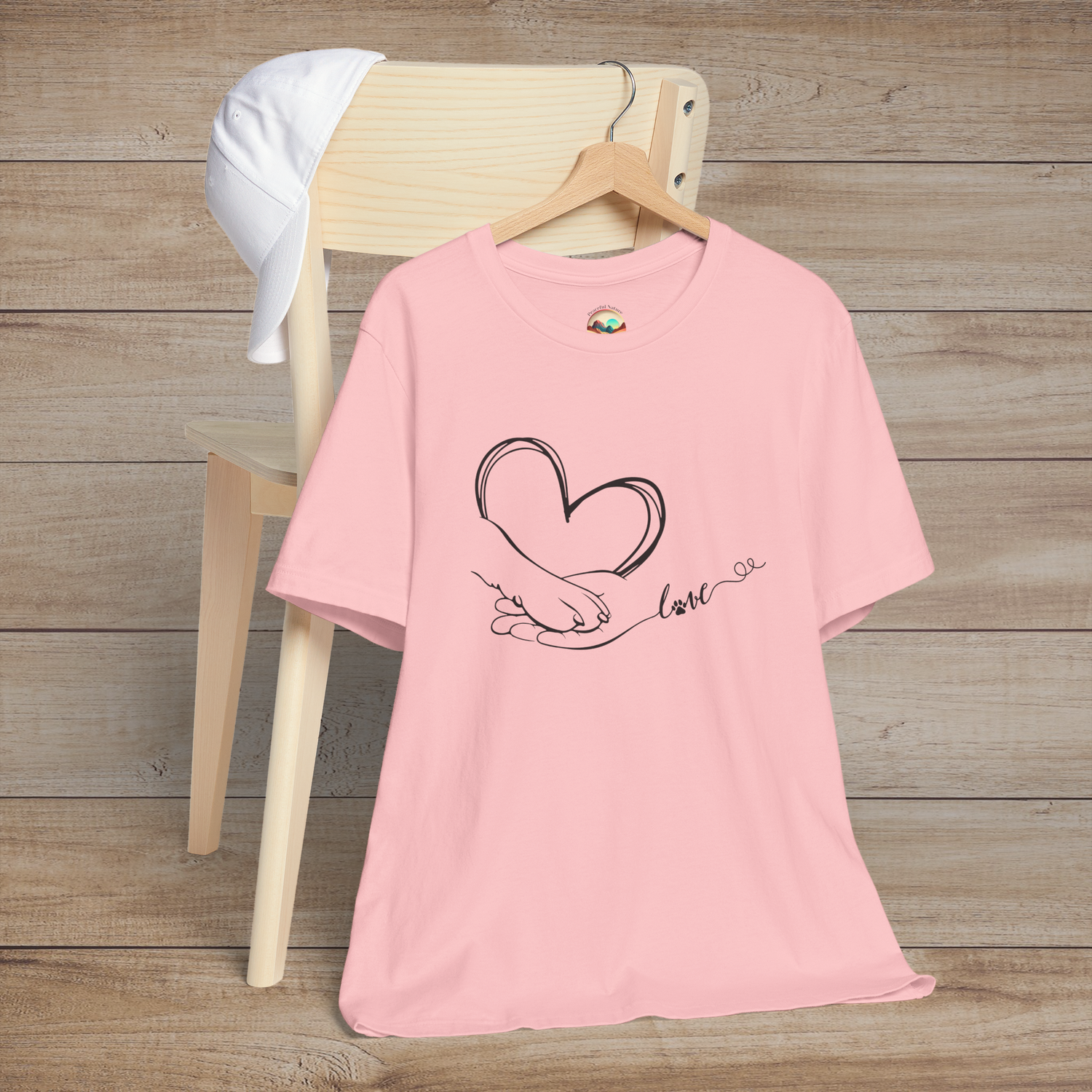 Pink t-shirt featuring clean black line art of a heart created by a human hand and a paw, connected by love script