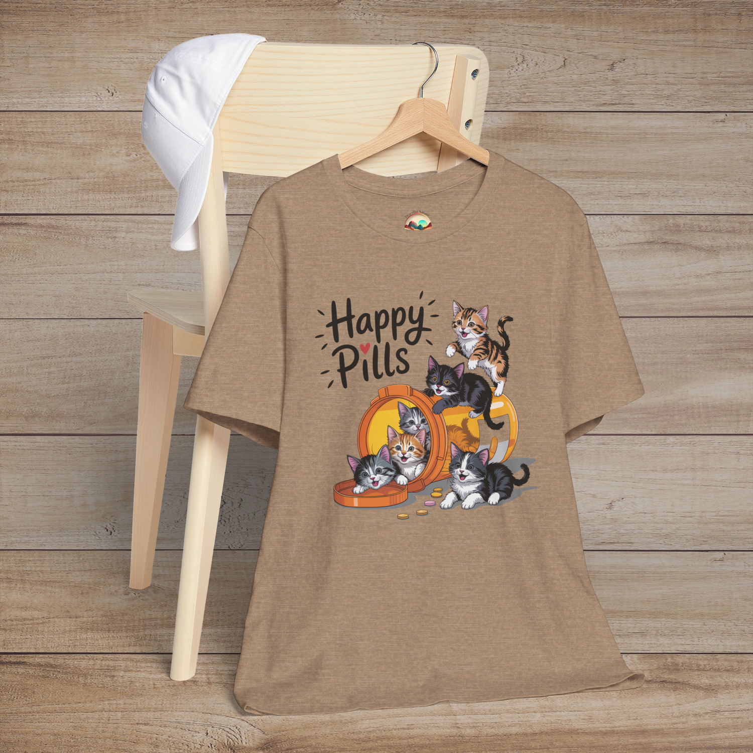 Happy Pills t-shirt on heather tan background, featuring playful kittens around an orange bottle