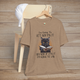 Heather tan Let God Fix It T-Shirt with a serious black cat holding a book and humorous faith-inspired message