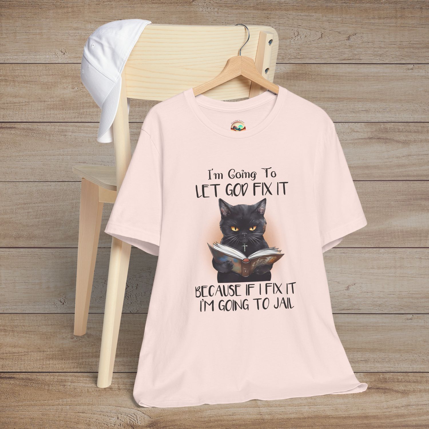 Soft pink Let God Fix It T-Shirt with a black cat wearing a necklace and reading a book with a humorous Christian quote