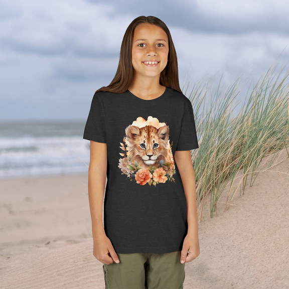 Young girl wearing a dark grey Lion Cub Floral Youth T-Shirt featuring a watercolor lion cub with flowers, standing by sand dunes and the ocean