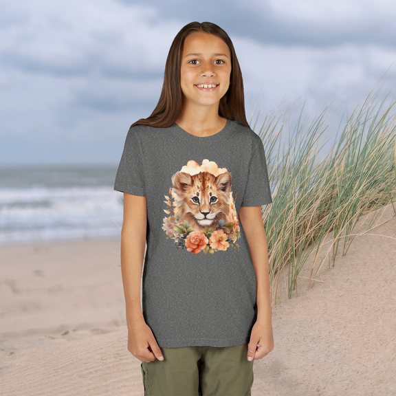 Young girl wearing a heather grey Lion Cub Floral Youth T-Shirt with a watercolor lion cub and flowers, standing on a beach