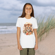 Youth girl wearing a white Lion Cub Floral Youth T-Shirt with a charming lion cub and floral watercolor design, sandy beach setting