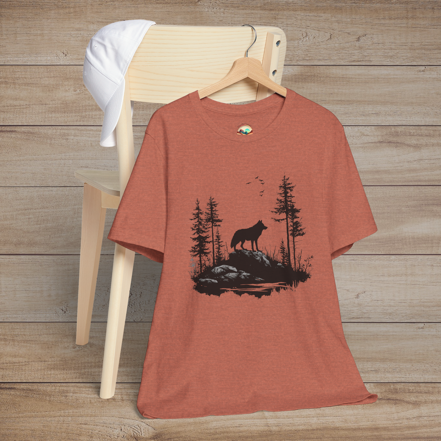 Heather clay t-shirt with a striking black silhouette of a lone wolf among evergreen trees and flying birds, symbolizing harmony with nature
