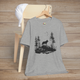 Heather grey t-shirt featuring a lone wolf howling on a rocky cliff surrounded by evergreen trees and flying birds, symbolizing strength and independence