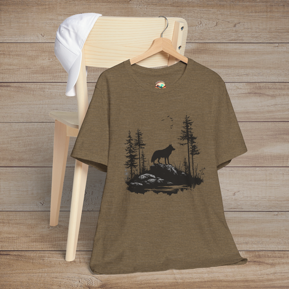 Heather olive t-shirt depicting a silhouette of a lone wolf on rugged rocks among dense trees, with birds overhead, creating a peaceful wildlife scene