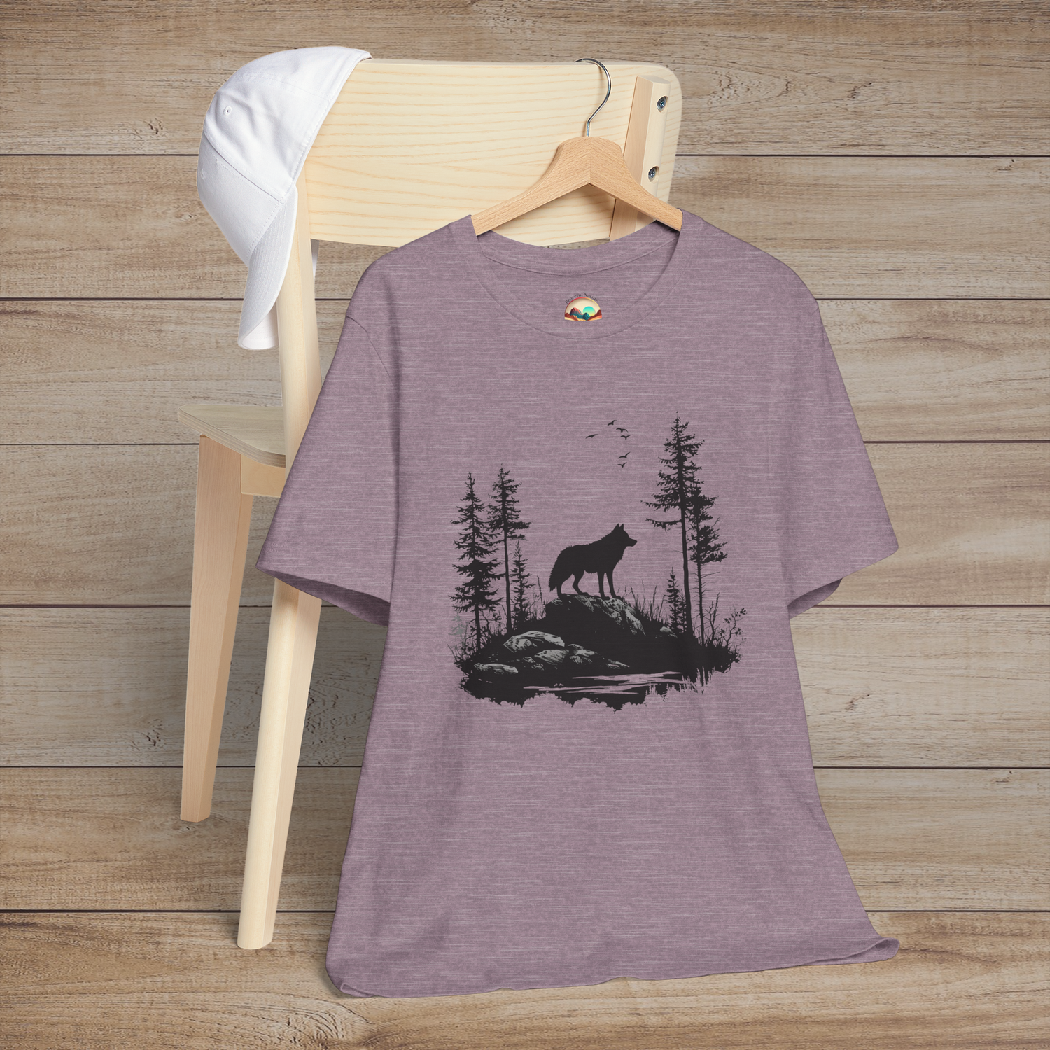 Heather purple t-shirt showcasing a lone wolf silhouetted against a wilderness backdrop of pine trees and birds, symbolizing resilience and solitude