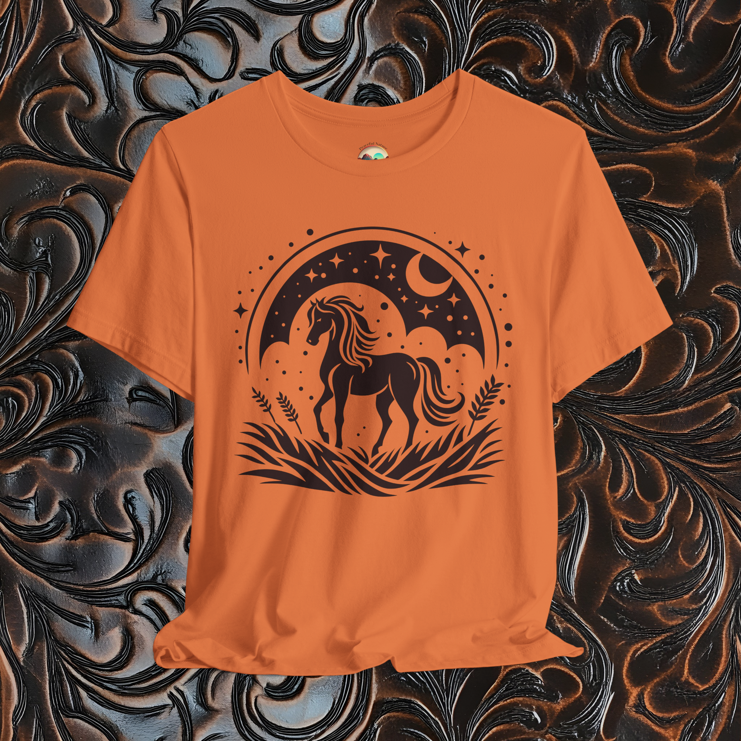 Flat lay of The Majestic Horse T-shirt in burnt orange with celestial horse design on rustic background