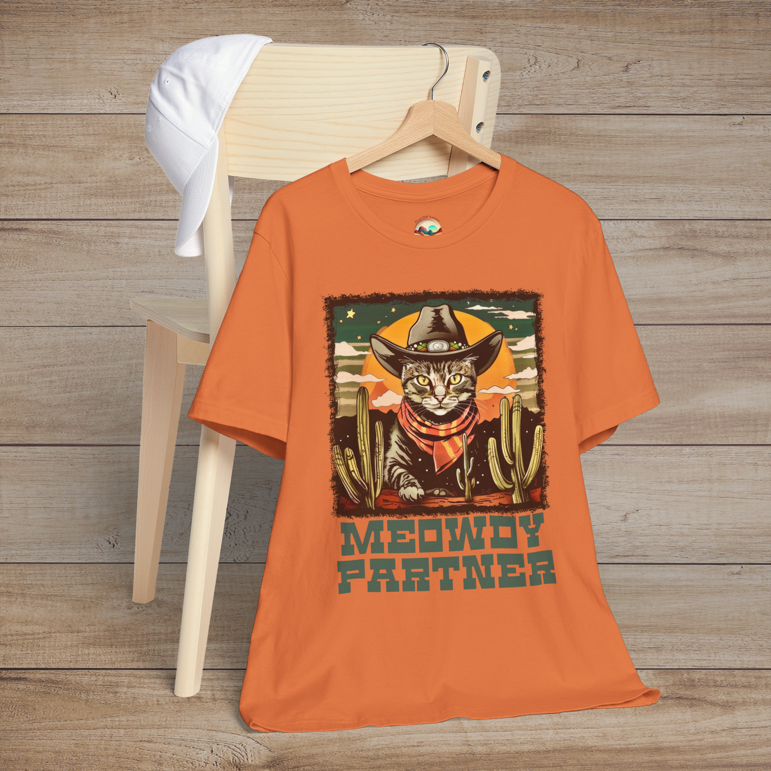 Burnt Orange Meowdy Partner Cowboy Cat Tee showcasing a humorous feline cowboy scene complete with hat, scarf, and desert cacti