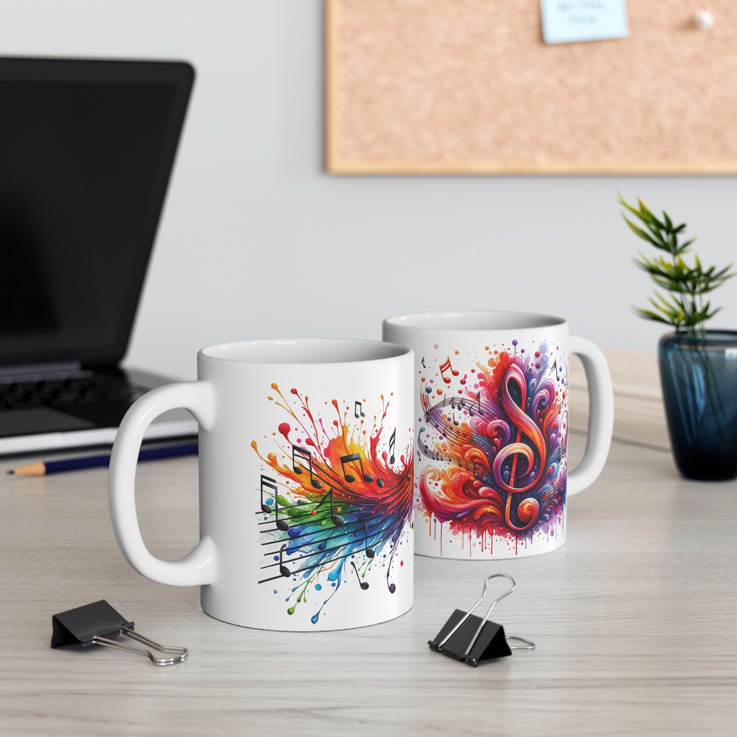 The Musical Notes Watercolor Mug shown on both sides, with one side displaying a colorful treble clef and the other a burst of musical notes in watercolor style, placed on a work desk