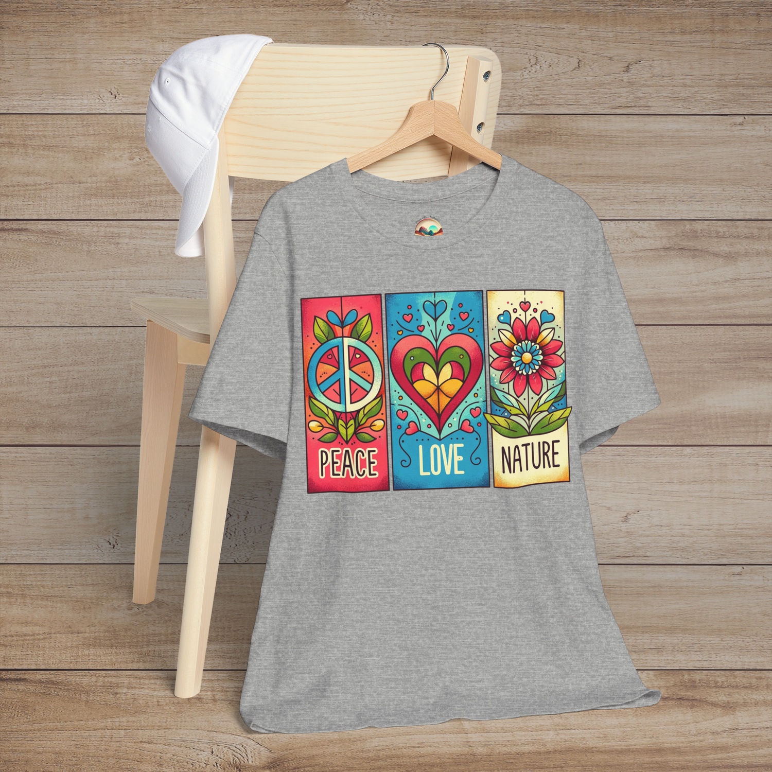 Heather grey Peace Love and Nature T-Shirt hanging on a chair, showcasing a colorful retro design with peace, love, and flower graphics. Ideal soft-fit tee for those who love earthy tones and bohemian vibes