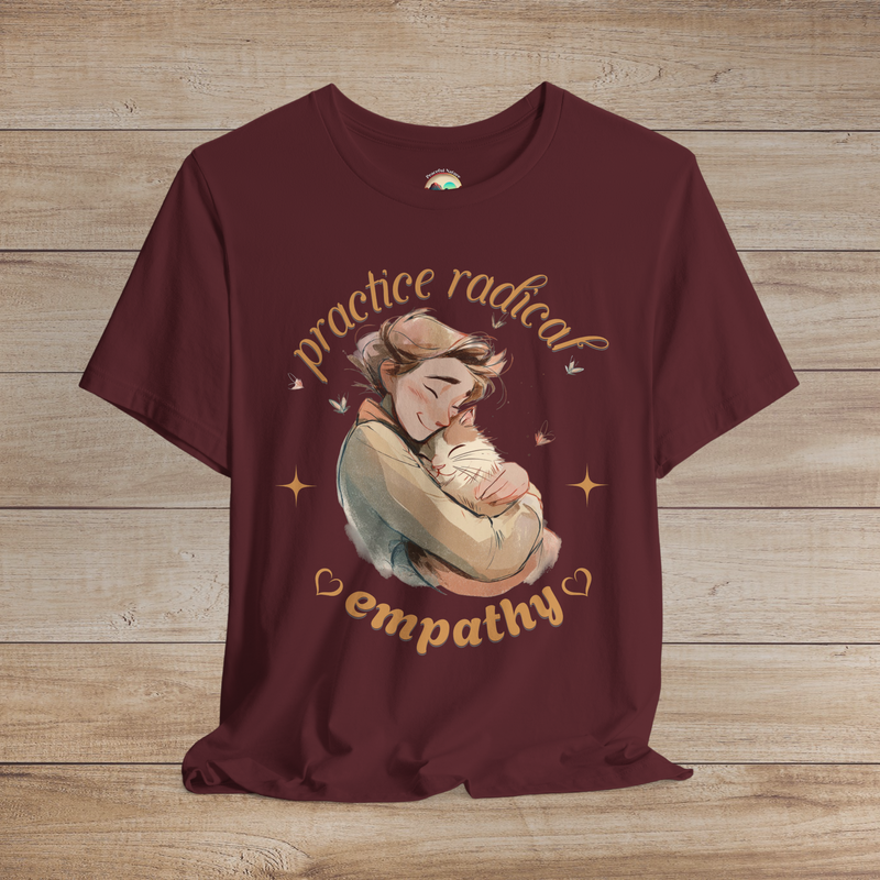 Maroon t-shirt showing a peaceful illustration of a cat being hugged by a smiling person, surrounded by butterflies and text saying “Practice Radical Empathy.”