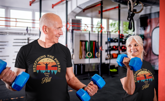 Older man and woman wearing black "Over the Hill" t-shirts lifting blue dumbbells at the gym