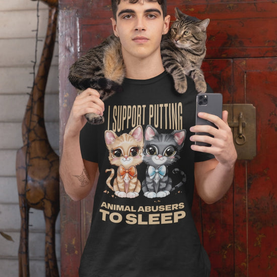 Video of man wearing a black t-shirt with cat graphics and animal advocacy text, holding a phone, with a cat on his shoulder.