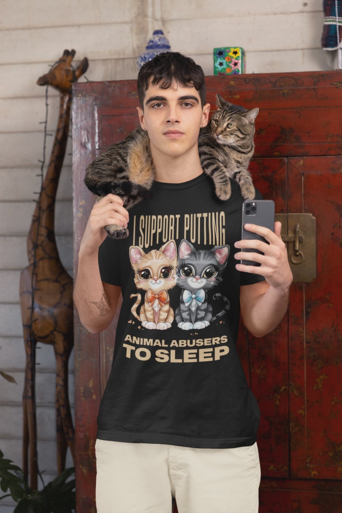 Video of man wearing a black t-shirt with cat graphics and animal advocacy text, holding a phone, with a cat on his shoulder.