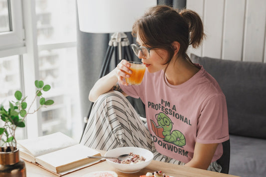 Video of woman wearing the heather mauve t-shirt with a graphic and text 'I'm a Professional Bookworm' on a wooden chair.
