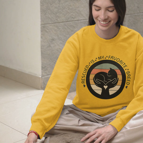 Video of woman who is wearing the Rescued is My Favorite Breed Gildan 18000 sweatshirt in Gold. The woman is petting a cat. 