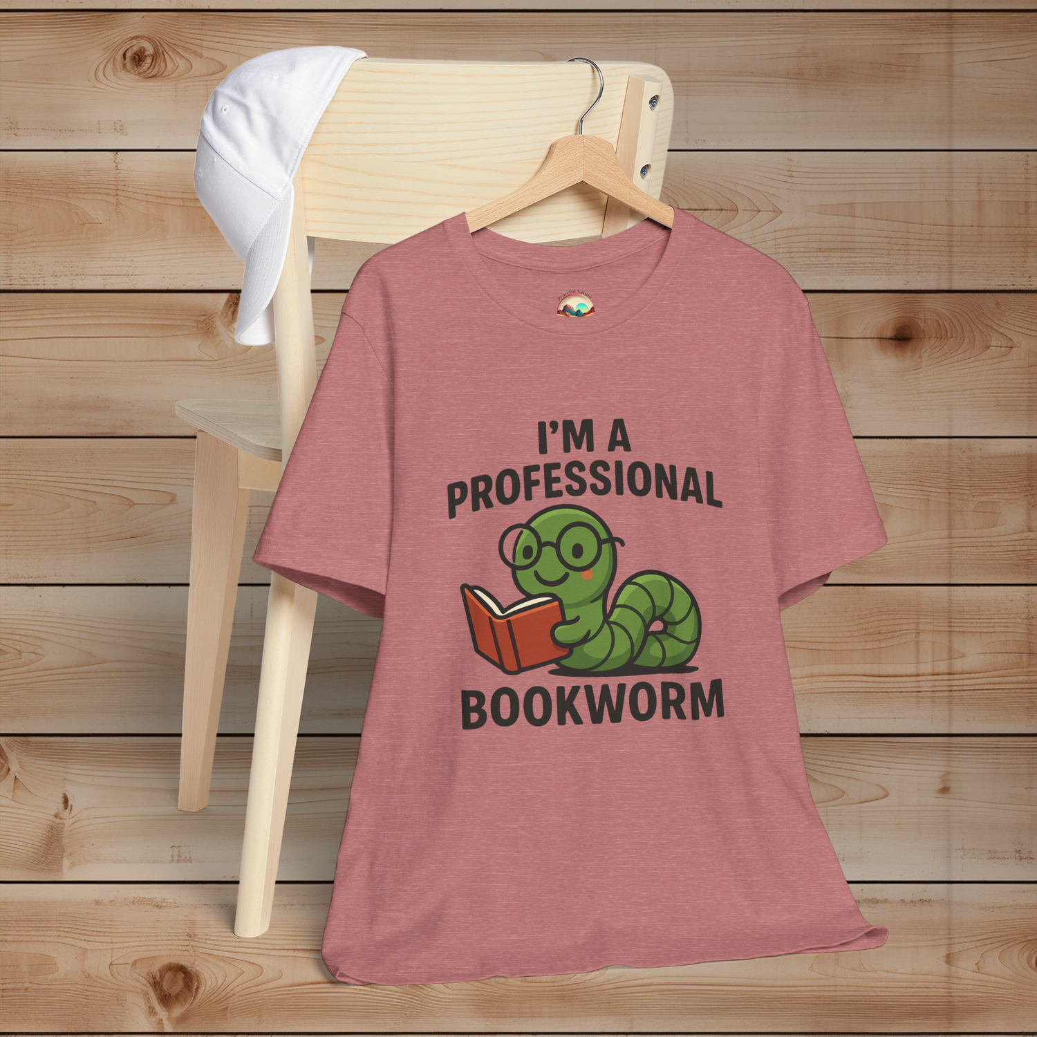 Heather mauve t-shirt with a graphic and text 'I'm a Professional Bookworm' on a wooden chair.