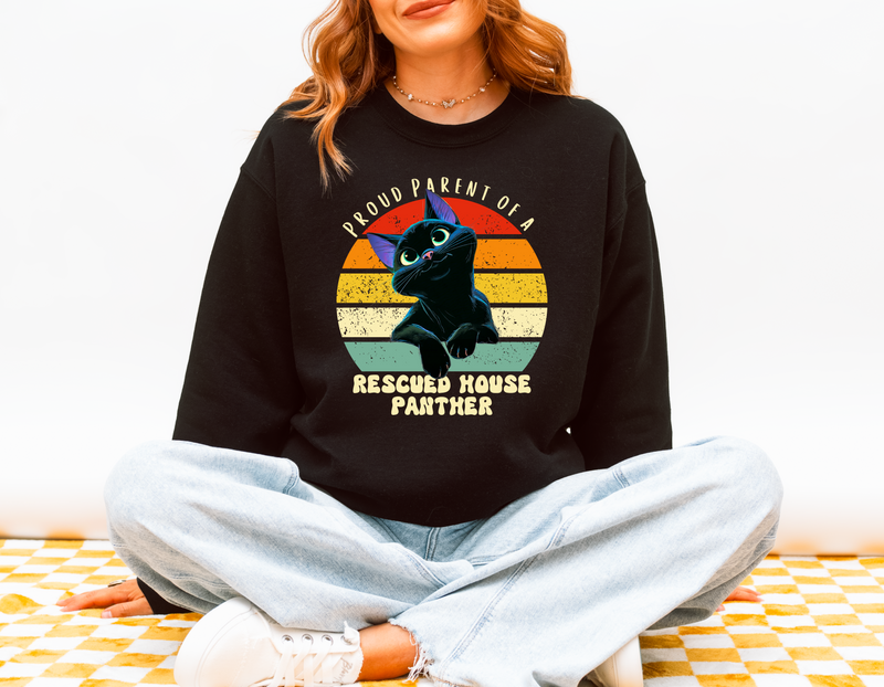 Model wearing a black Gildan 18000 sweatshirt with a retro design reading Proud Parent of a Rescued House Panther and a black cat illustration