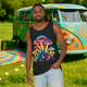 Front view of unisex psychedelic mushroom tank top on a man, featuring vibrant neon mushroom design – set against a retro VW bus and colorful outdoor setting.