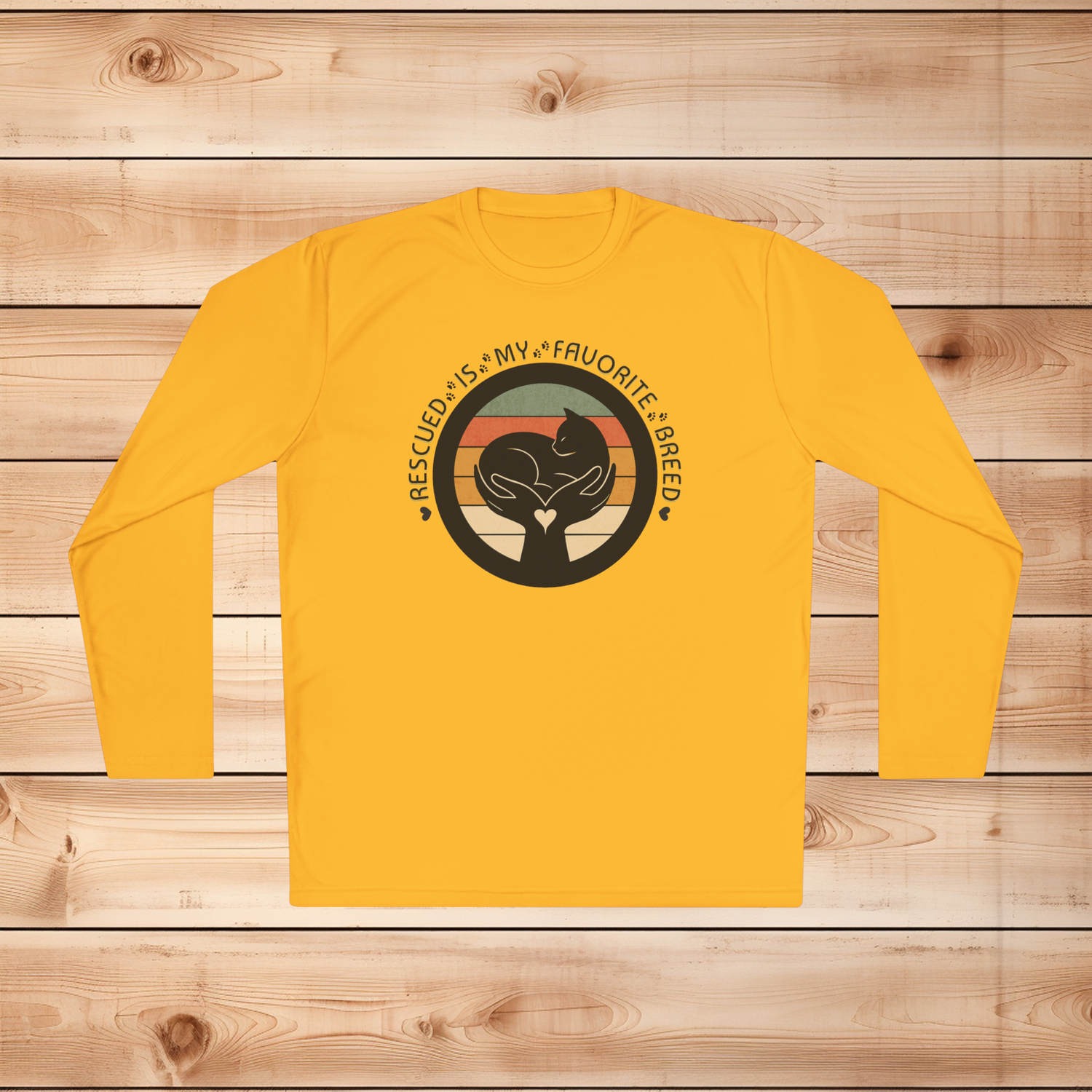 Gold Sport-Tek long sleeve shirt with text saying "Rescued Is My Favorite Breed," with a black and white graphic on a wooden background
