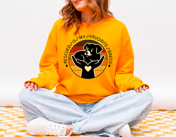 Model seated cross-legged wearing gold Gildan 18000 Rescued Is My Favorite Breed sweatshirt with retro sunset dog rescue graphic