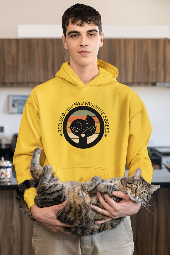Man wearing a daisy yellow 'Rescued Is My Favorite Breed' retro cat rescue hoodie while holding a relaxed tabby cat.