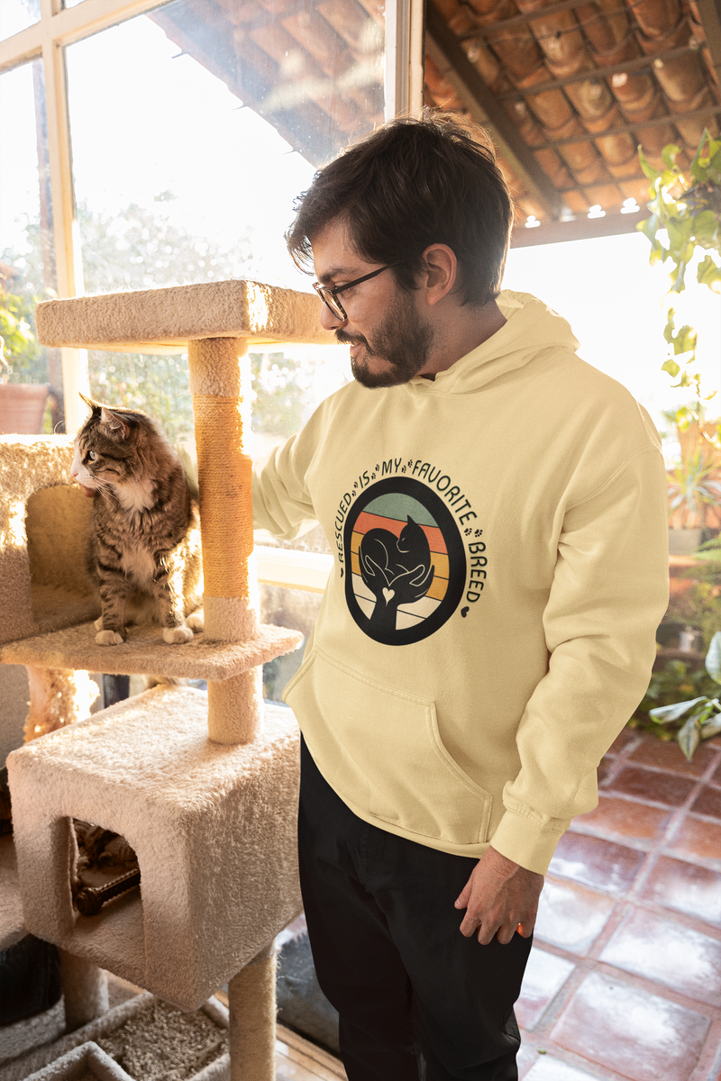 Bearded man wearing a butter yellow 'Rescued Is My Favorite Breed' retro cat rescue hoodie while petting his cat near a cat tree