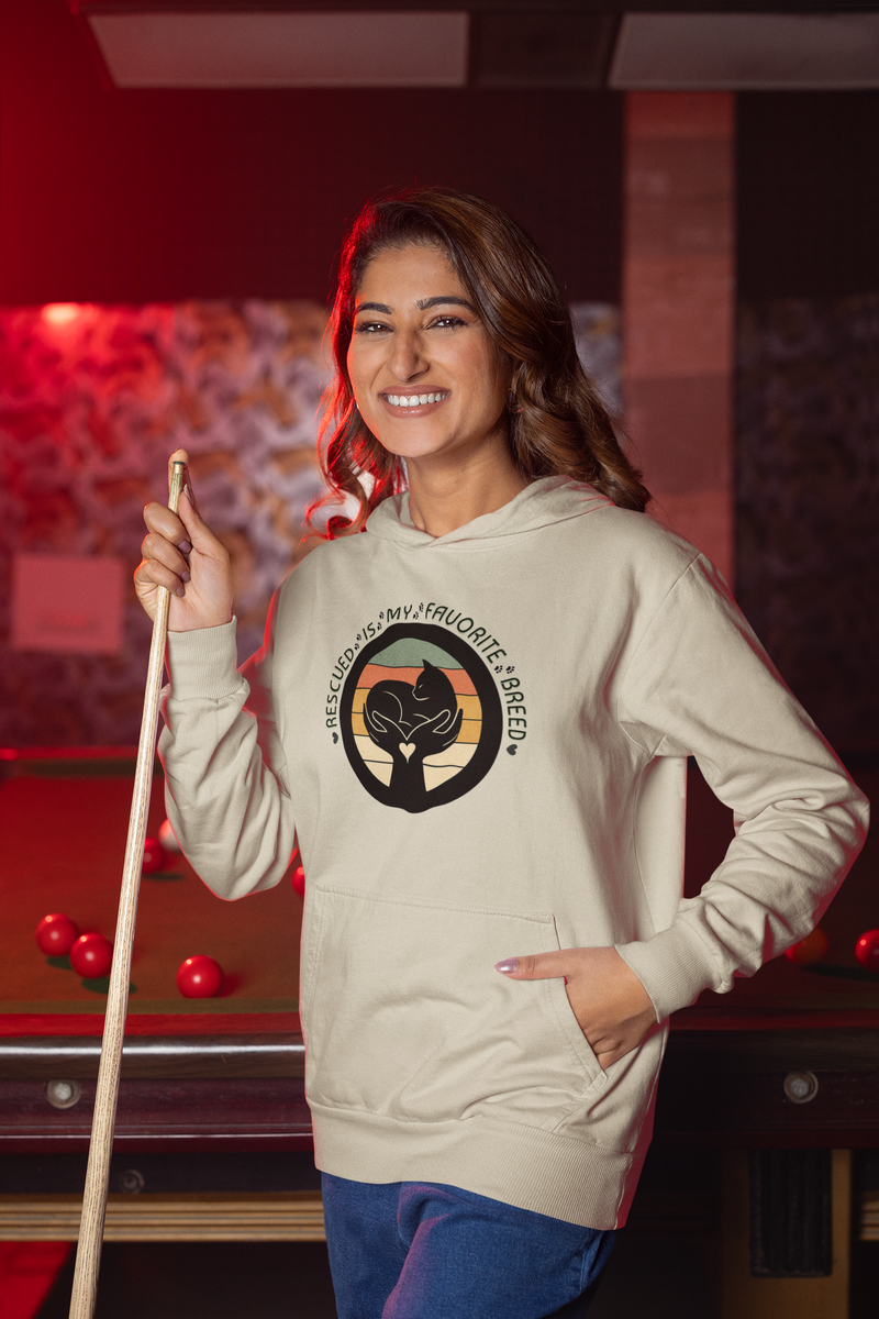 Cheerful woman playing pool while wearing a sand-colored 'Rescued Is My Favorite Breed' retro cat rescue hoodie