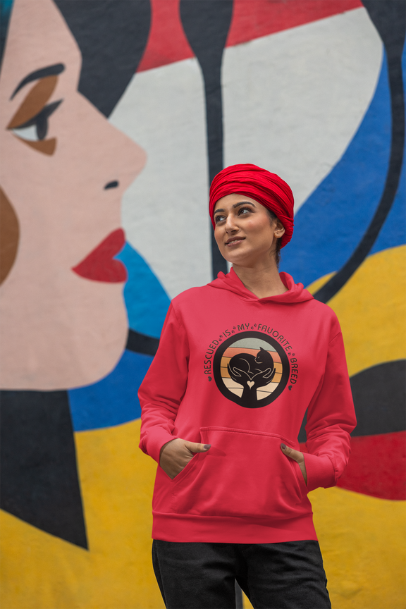 Happy woman wearing a red 'Rescued Is My Favorite Breed' retro cat rescue hoodie and a matching red turban in front of a mural