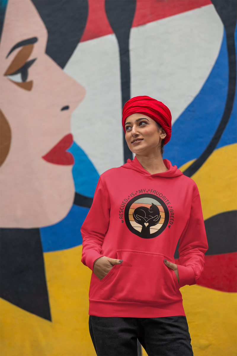 Happy woman wearing a red 'Rescued Is My Favorite Breed' retro cat rescue hoodie and a matching red turban in front of a mural
