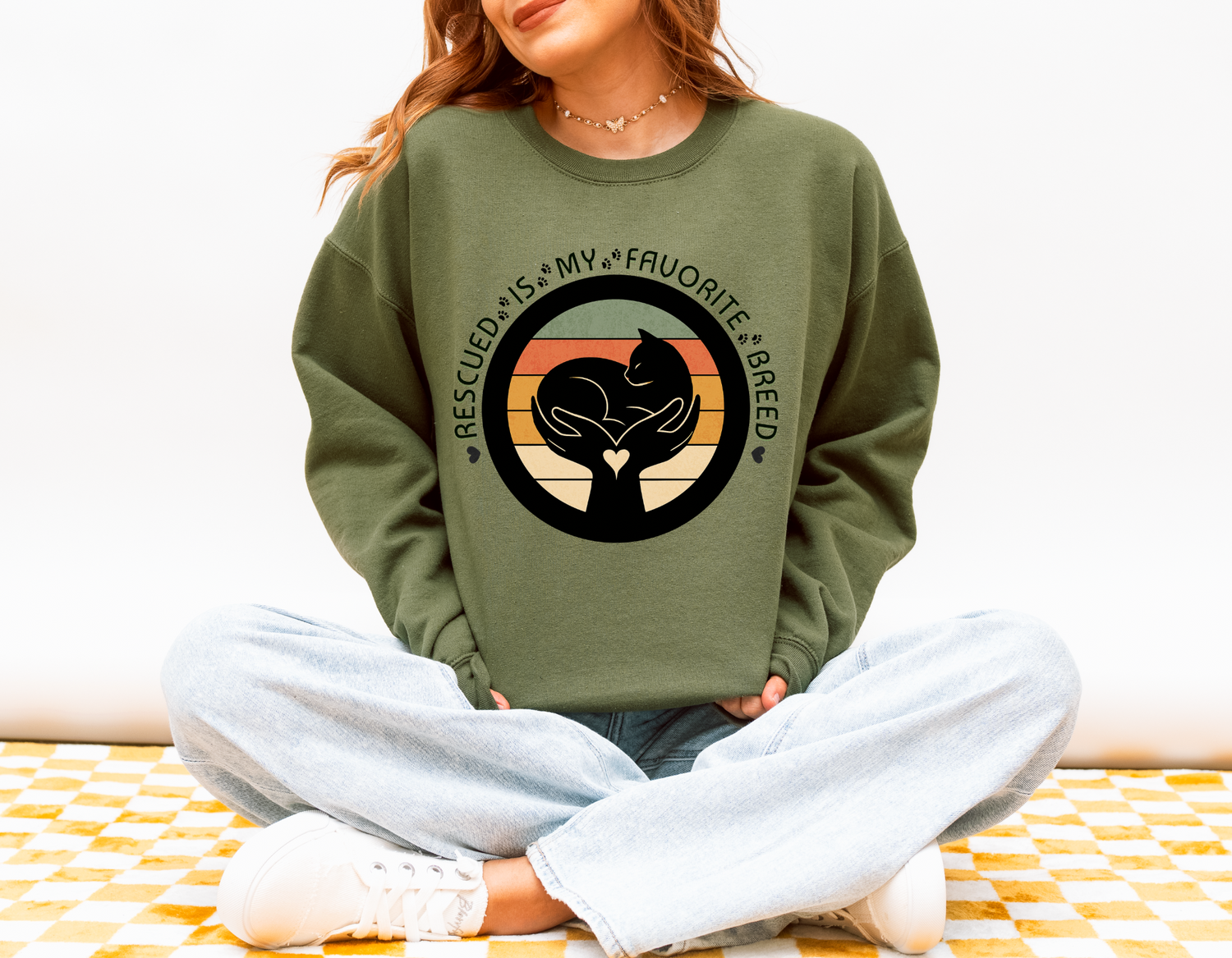 Model in military green Rescued Is My Favorite Breed sweatshirt featuring retro circle cat and hand design supporting pet adoption