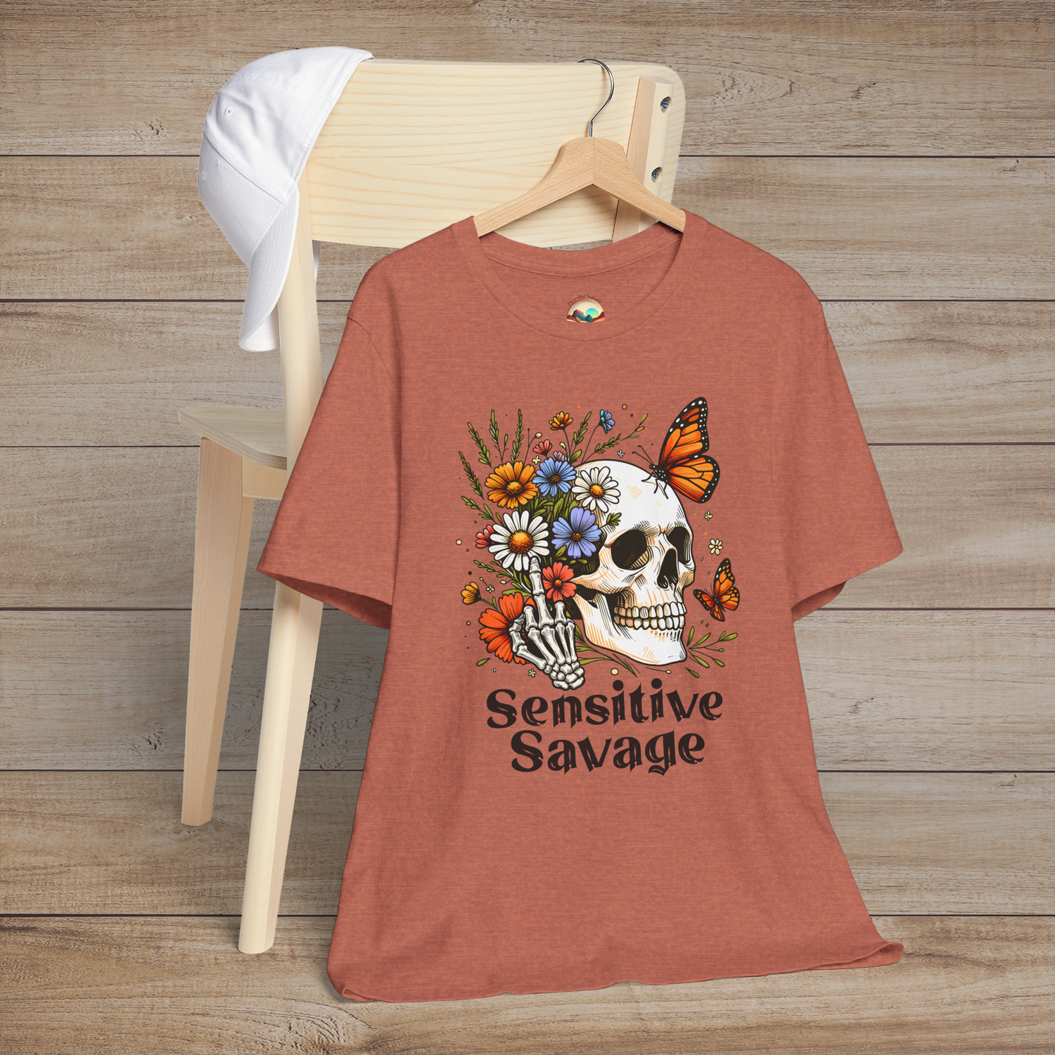 Heather clay t-shirt showing a skull, skeleton hand, vibrant flowers, butterflies, and Sensitive Savage written underneath