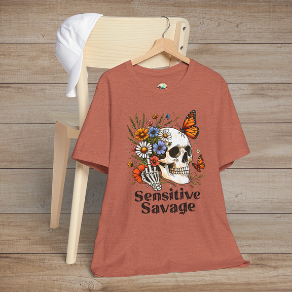 Heather clay t-shirt showing a skull, skeleton hand, vibrant flowers, butterflies, and Sensitive Savage written underneath