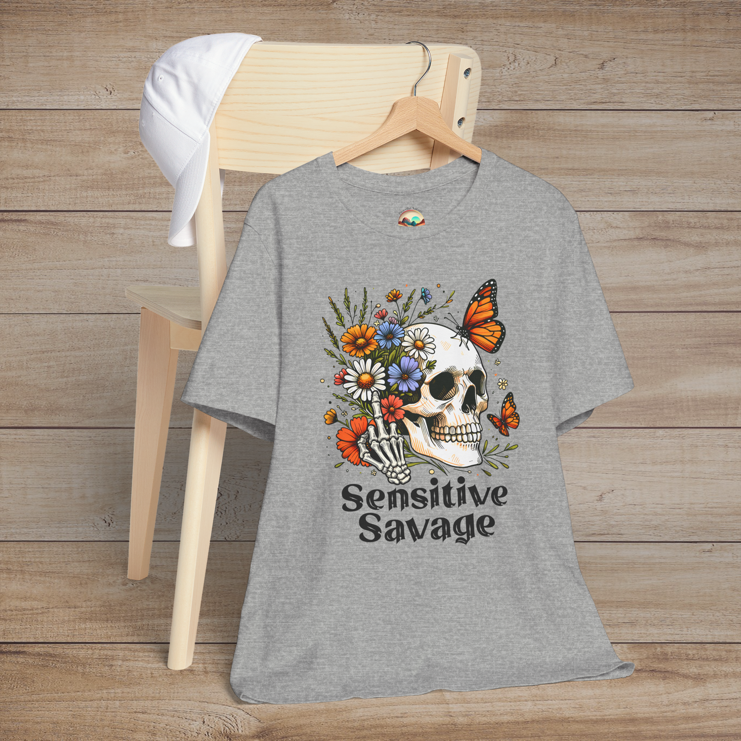 Heather gray t-shirt featuring a skull with a skeleton hand holding colorful flowers and butterflies with the text Sensitive Savage