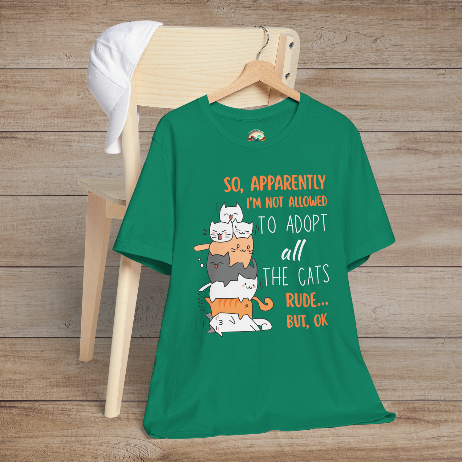 Kelly green shirt featuring a playful cartoon cat stack and the phrase “So apparently I’m not allowed to adopt all the cats… Rude, but OK.”
