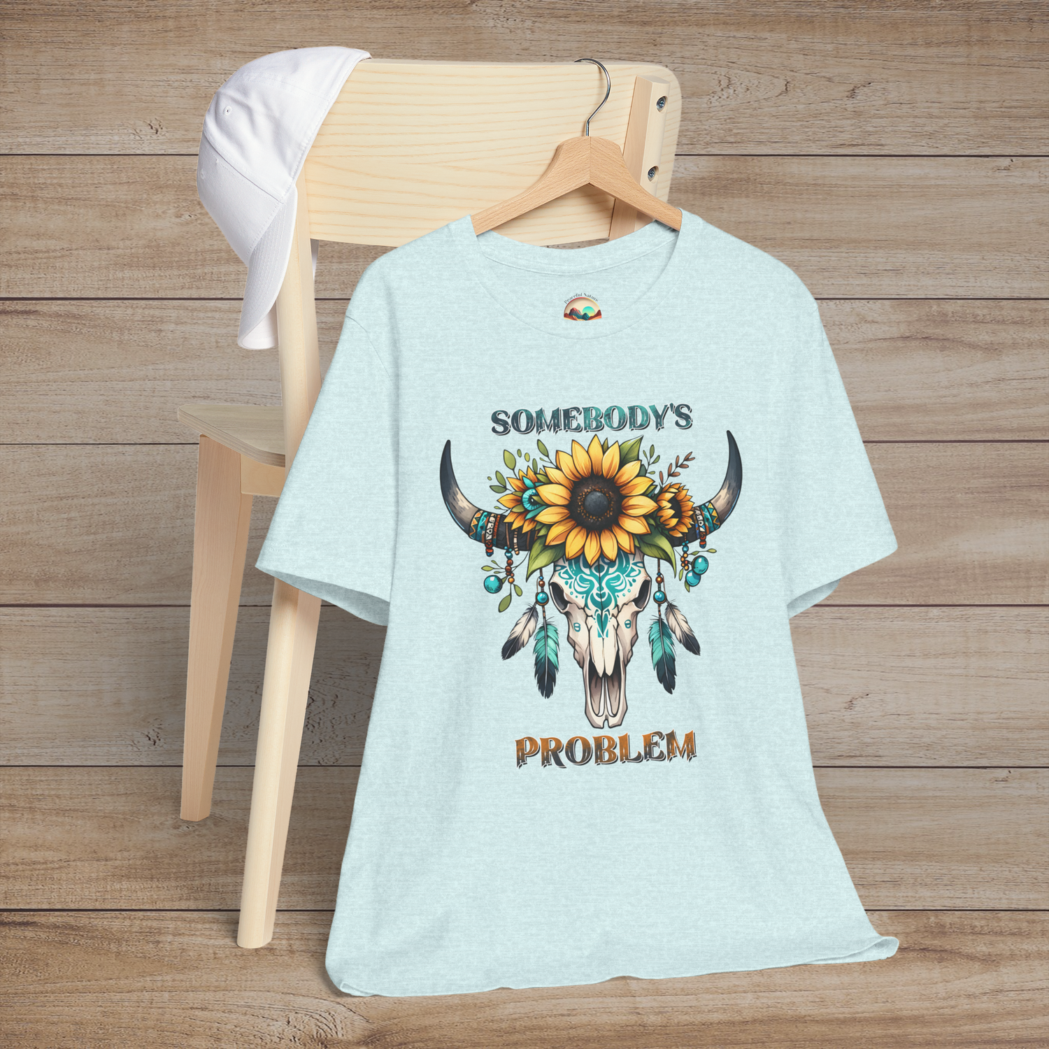 Somebody’s Problem T-Shirt showing a detailed western skull with colorful Boho accents on heather prism ice blue fabric