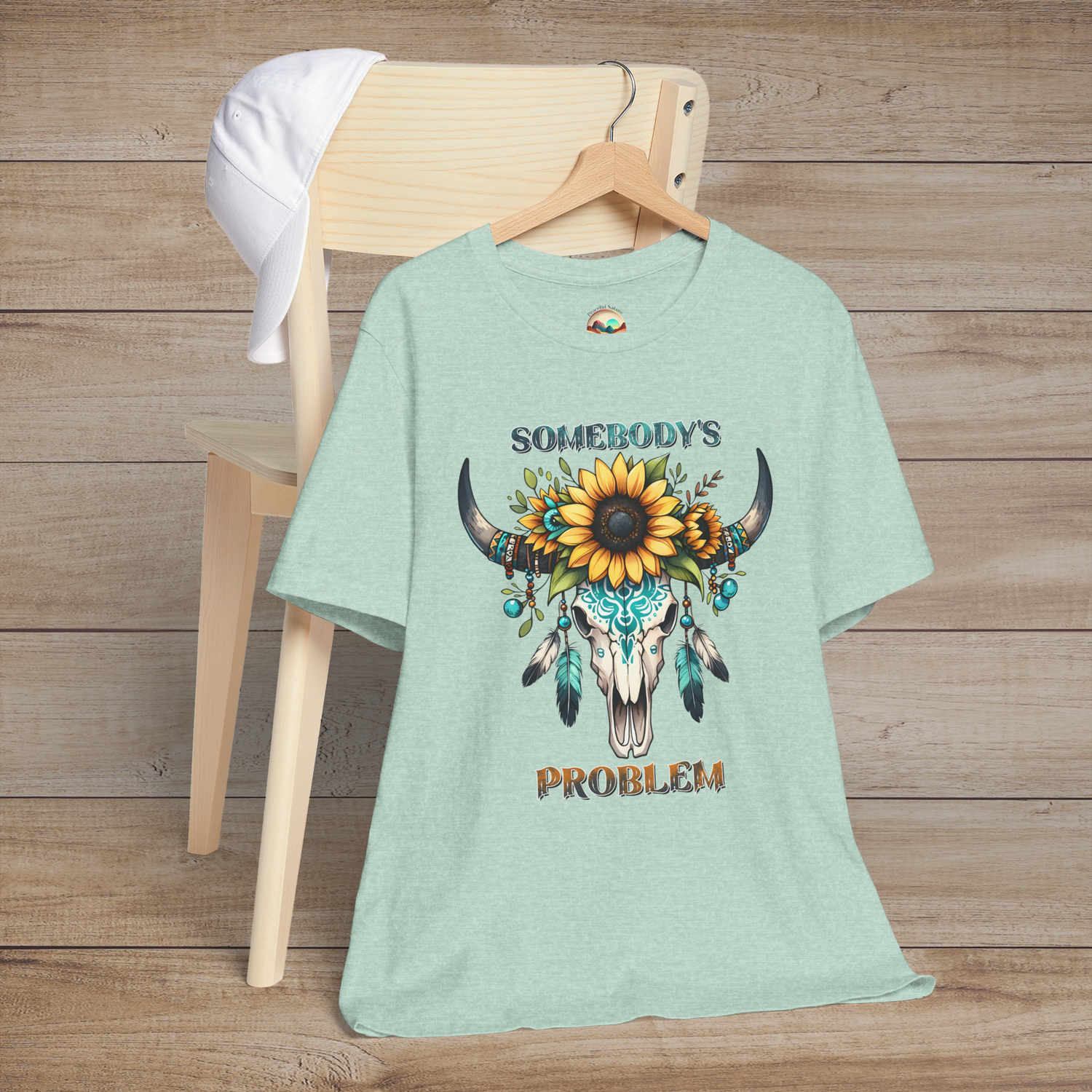 Somebody’s Problem T-Shirt featuring a stylish Bohemian skull graphic with sunflowers and turquoise feathers on heather prism mint fabric