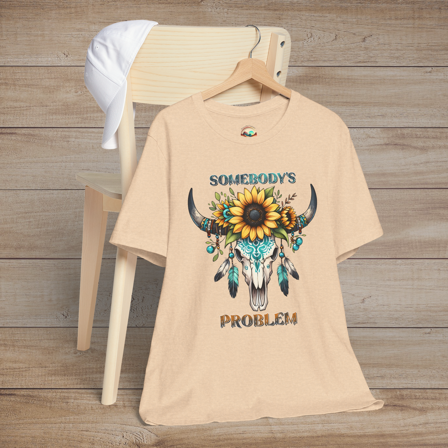 Somebody’s Problem T-Shirt with a striking Boho western skull, sunflower crown, and turquoise details on heather sand dune fabric