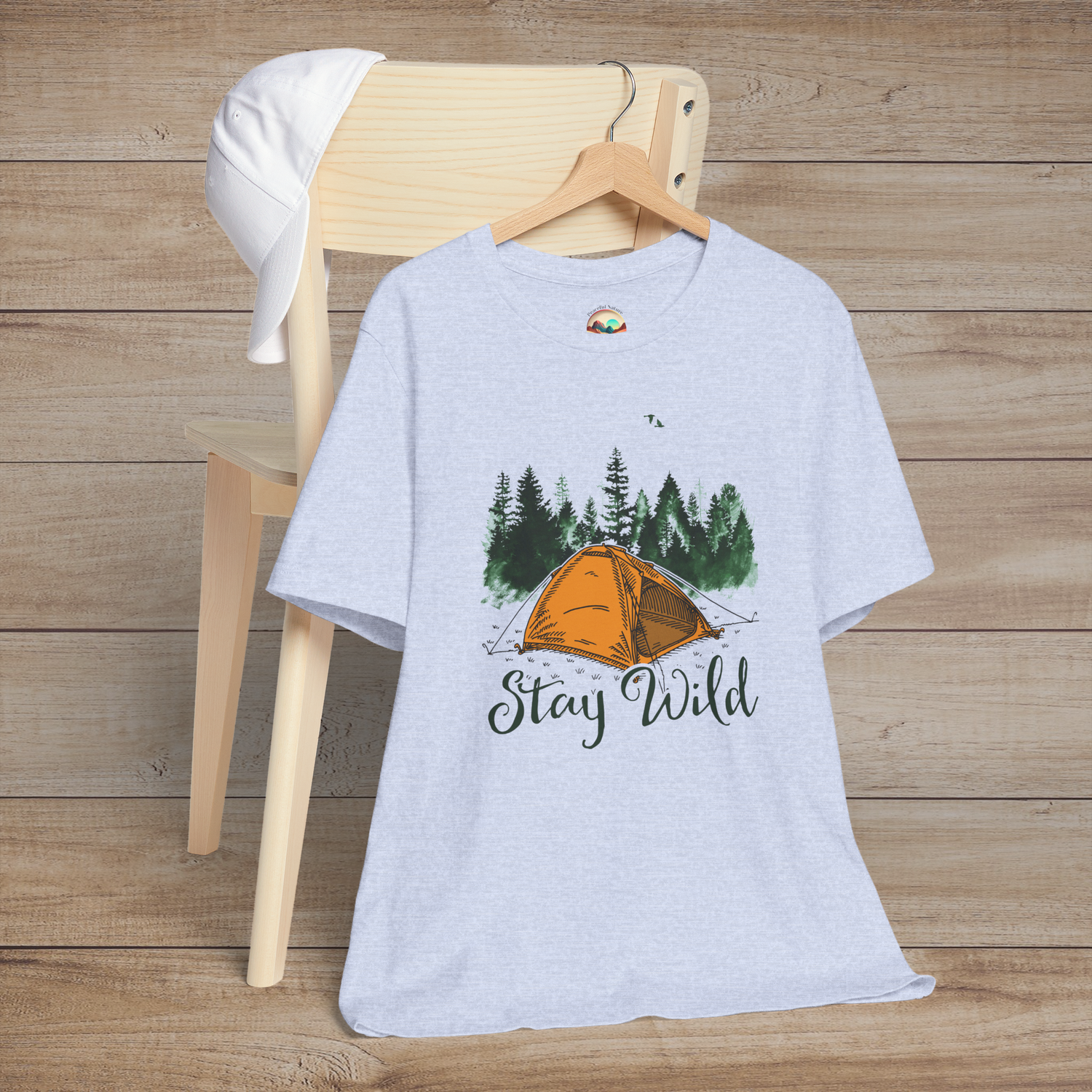 Heather blue Stay Wild Camper T-Shirt featuring an orange tent, evergreen trees, and birds with "Stay Wild" text