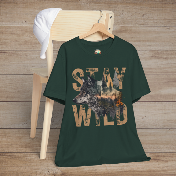 Dark forest green T-shirt with "Stay Wild" text and a scenic wolf and pine forest graphic in the middle, laid out on a chair for a cozy, woodland vibe