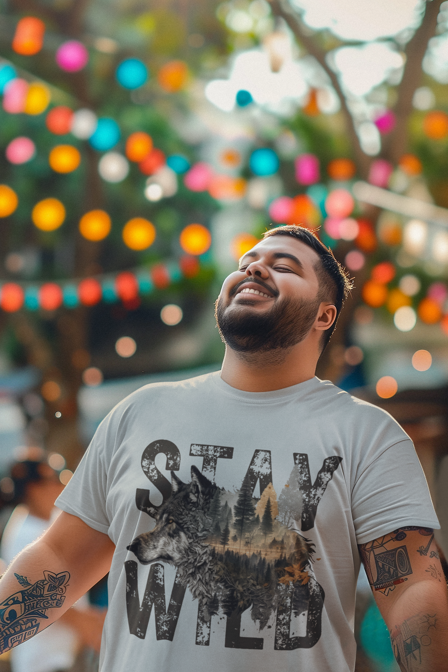 Man smiling under colorful lanterns, wearing the Stay Wild wolf t-shirt in heather grey