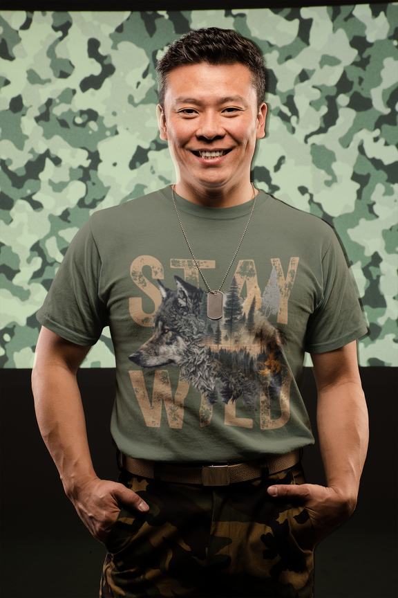 Man in front of camouflage wall, wearing the Stay Wild wolf t-shirt in military green with dog tags